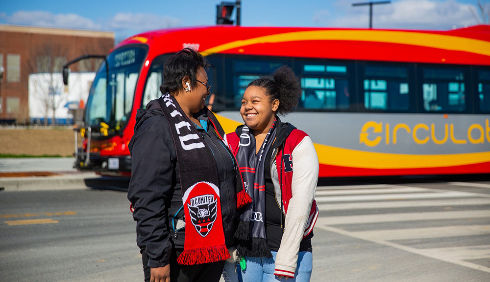 Two happy women standing outside a DC Circulator sports bus