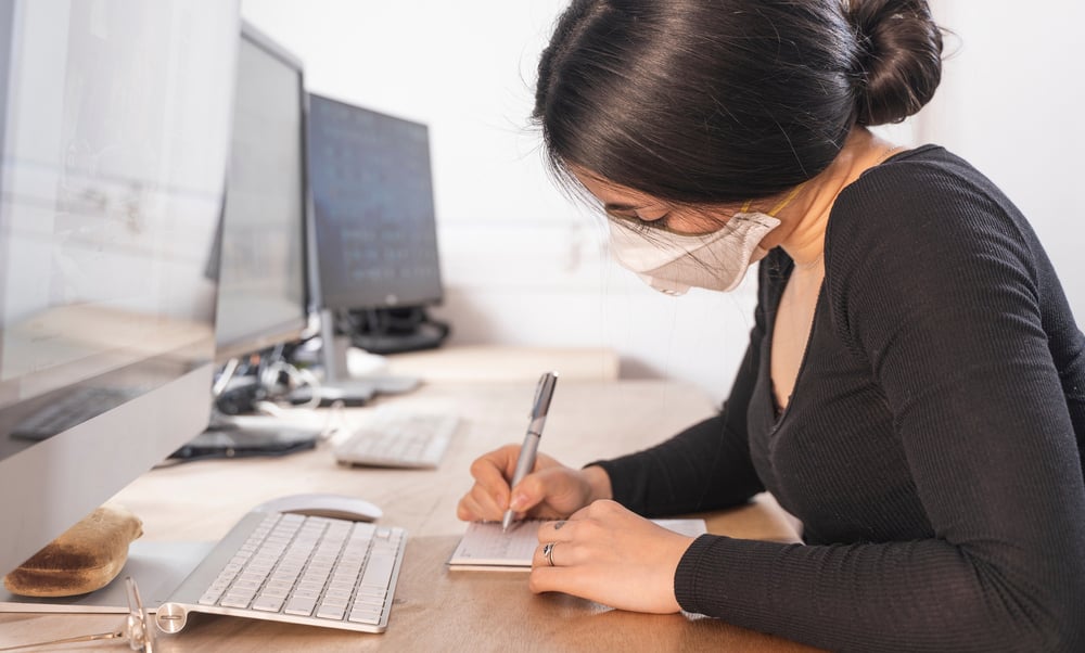 Woman taking notes at a computer with face mask on